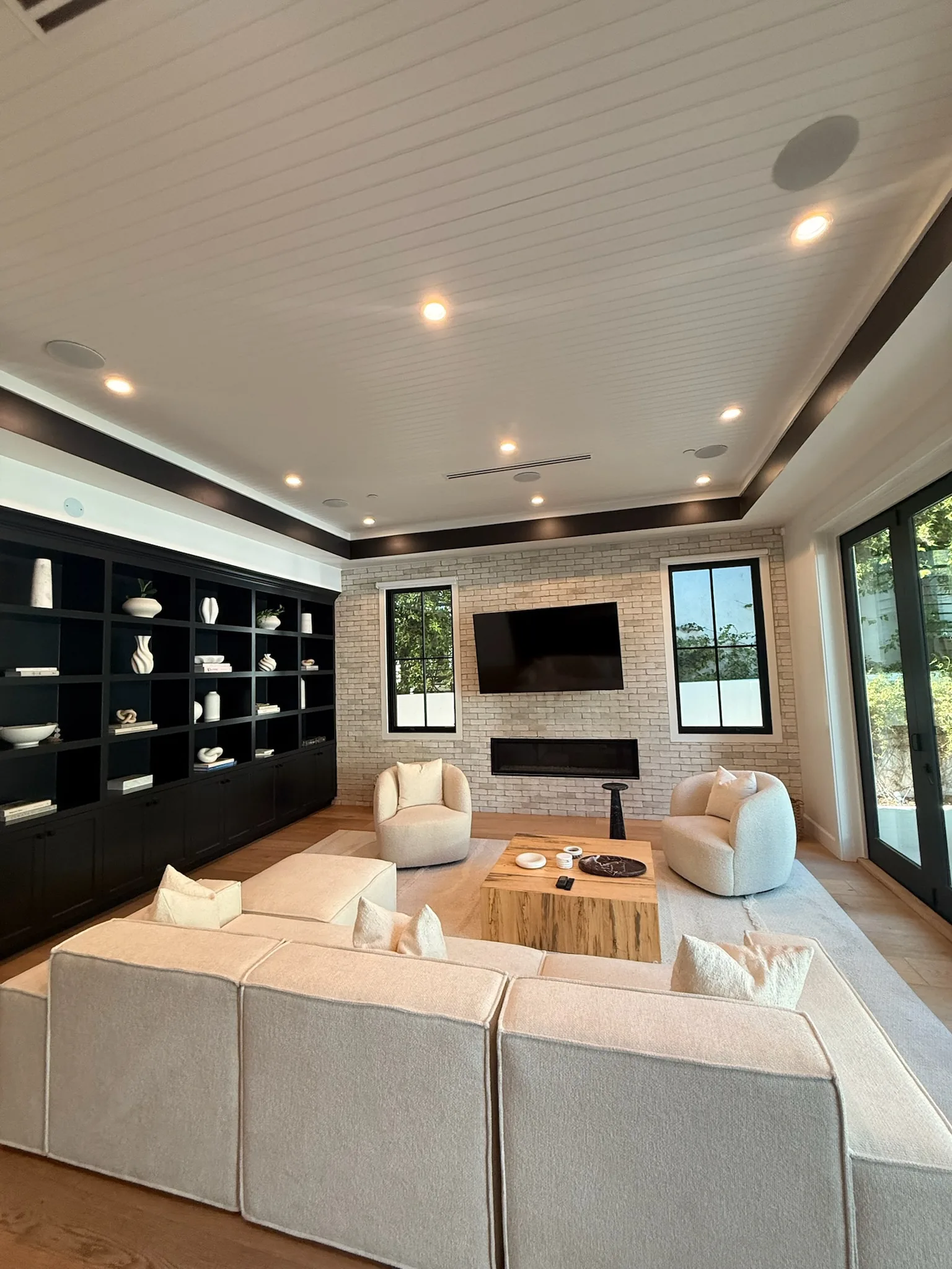 Bright living room with a white brick fireplace wall, black built-in shelving and cream seating